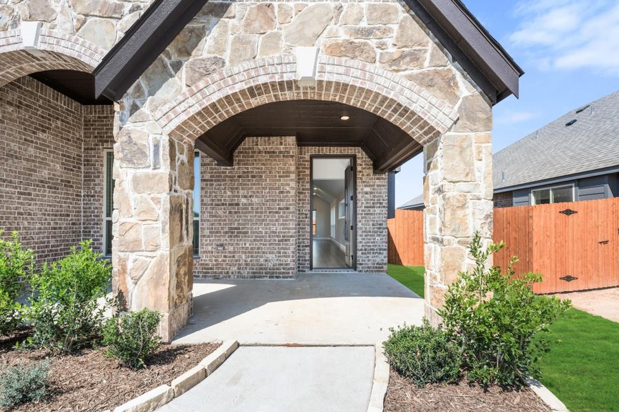 Covered front entry with stone and brick arched porch, concrete walkway, and landscaped shrubs Covered front entry with stone and brick arched porch, concrete walkway, and landscaped shrubs