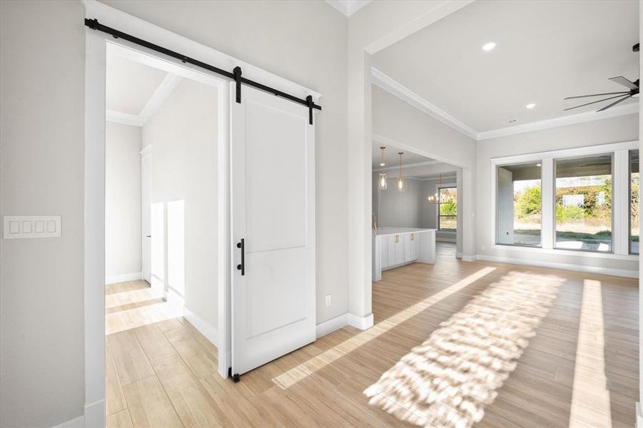 Hallway featuring a barn door, light hardwood / wood-style flooring, an inviting chandelier, and crown molding