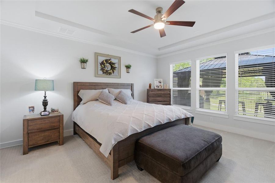 Primary bedroom featuring a tray ceiling with crown molding, a five-blade ceiling fan with integrated lighting, and white walls