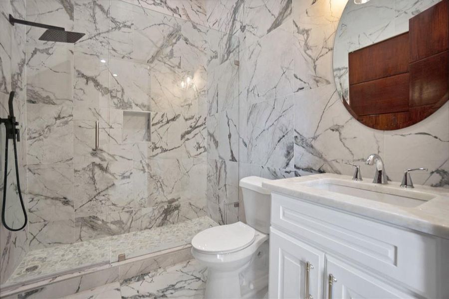 Bathroom featuring tiled shower, vanity, and toilet