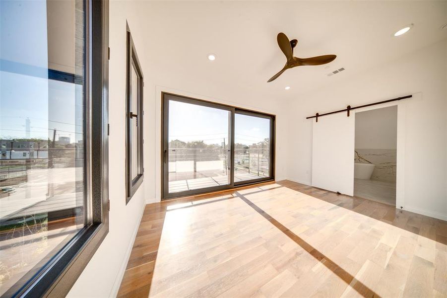 Spare room with a barn door, light wood-type flooring, and ceiling fan