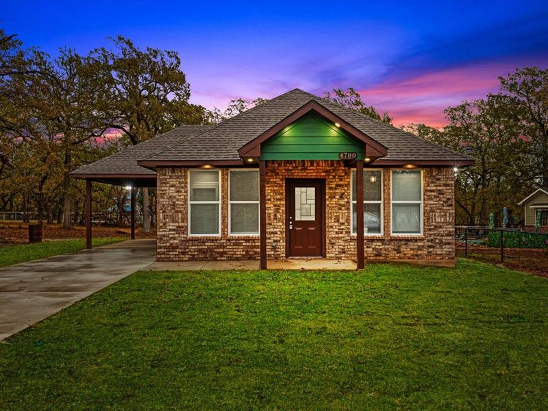 View of front facade with a lawn, concrete driveway, brick siding, and an attached carport