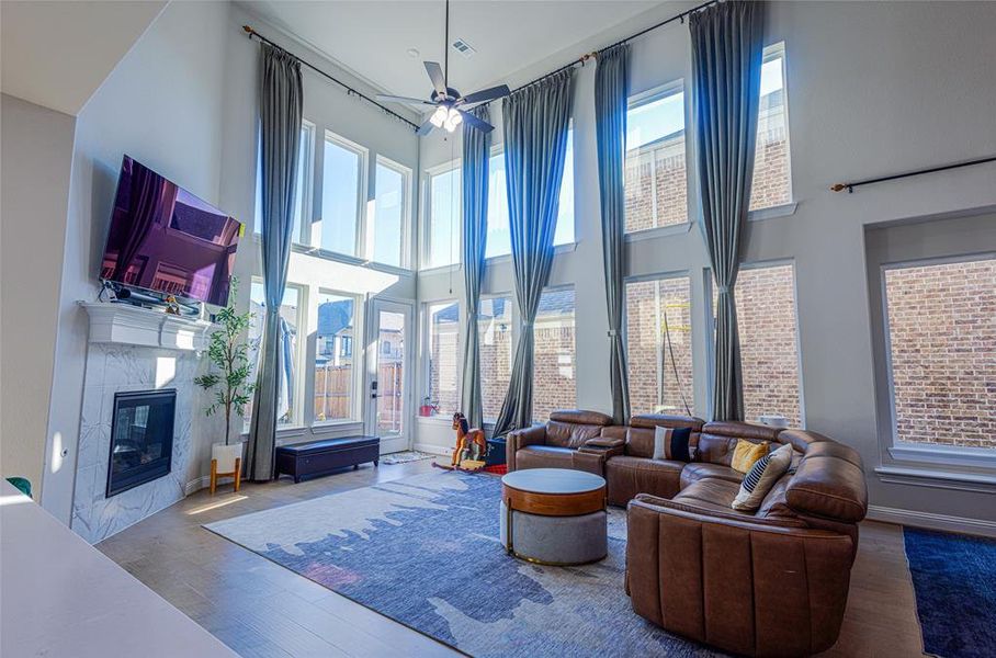 Living room featuring a premium fireplace, a ceiling fan, plenty of natural light, wood finished floors, and a high ceiling