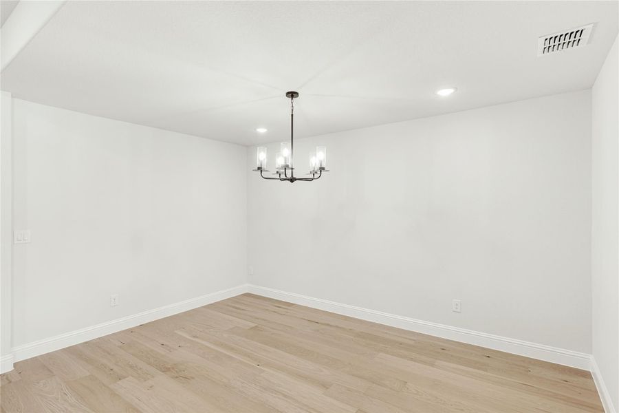 Empty dining room with light hardwood floors, white walls, and a black chandelier overhead.
