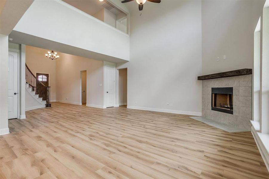 Unfurnished living room with ceiling fan with notable chandelier, light hardwood / wood-style flooring, a tile fireplace, and a high ceiling