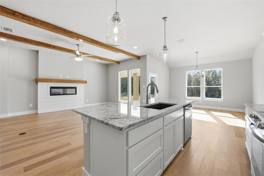 Kitchen with open floor plan, a glass covered fireplace, light stone counters, pendant lighting, and stove Kitchen with open floor plan, a glass covered fireplace, light stone counters, pendant lighting, and stove