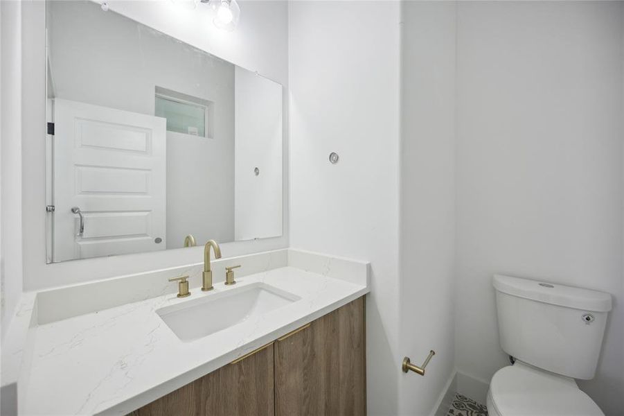 Modern powder room featuring a sleek vanity with white countertop and gold fixtures and oversized mirror. Enjoy a clean, bright space with a neutral color scheme!