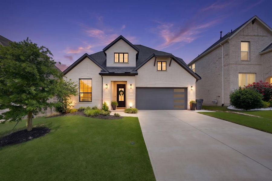 Contemporary exterior featuring light-colored brick, dark trim, a two-car garage with frosted glass inserts, a covered entry, and a manicured front lawn Contemporary exterior featuring light-colored brick, dark trim, a two-car garage with frosted glass inserts, a covered entry, and a manicured front lawn