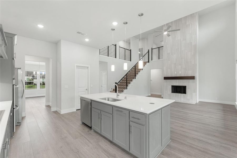Open kitchen with gray island, white countertops, and pendant lights, open to living area with staircase and fireplace
