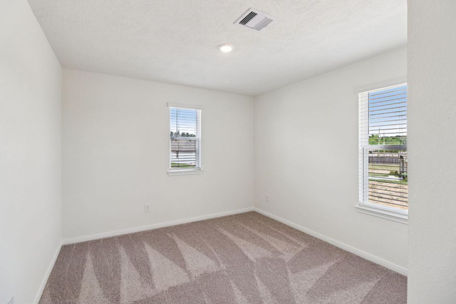 This secondary bedroom offers comfort and style with plush carpeting, neutral paint tones, recessed lighting, windows with blinds, and a generously sized closet.