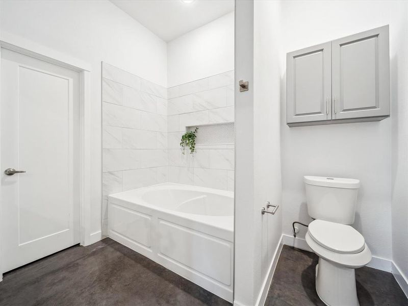 Bathroom with toilet, a tub, and concrete flooring