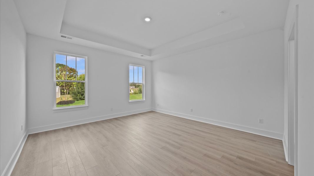 Elegant primary suite with hardwood flooring, tray ceiling, and superior natural light in this accomplished DRB Homes design Elegant primary suite with hardwood flooring, tray ceiling, and superior natural light in this accomplished DRB Homes design