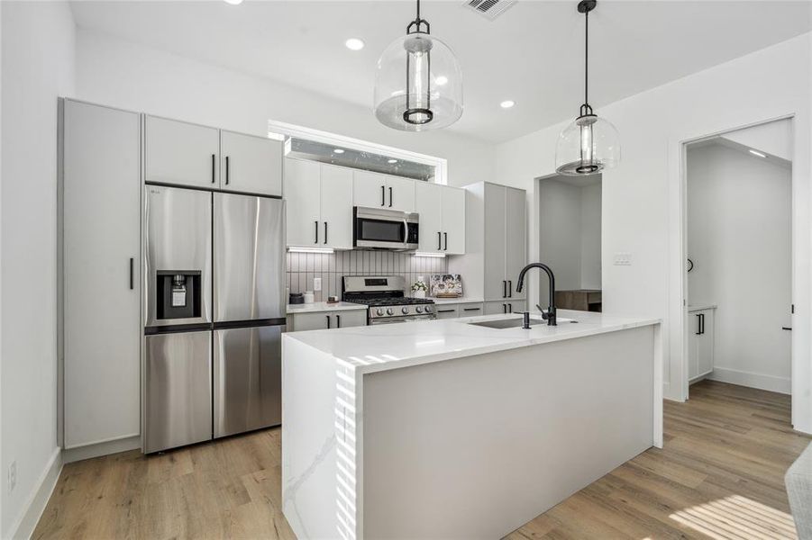 The kitchen showcases a new Vecino touch with slim shaker cabinets, oversized designer pendants with a clean quartz waterfall island counter.