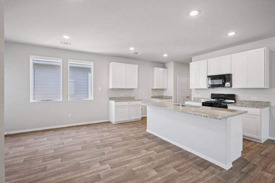 Image of a dining and kitchen area with grey walls, brown vinyl flooring, two windows, and white kitchen cabinets