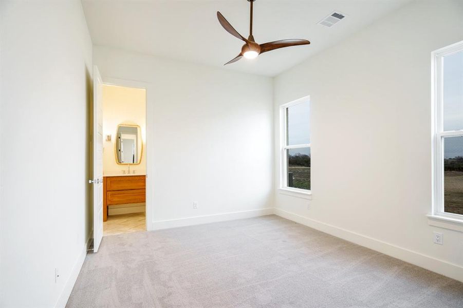 Unfurnished bedroom featuring light colored carpet, ensuite bath, and ceiling fan