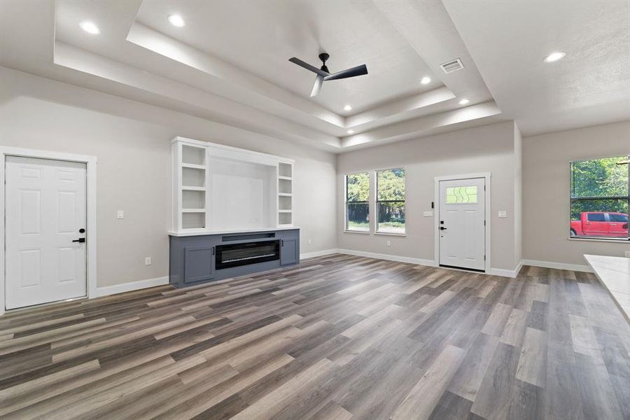 Unfurnished living room with a raised ceiling, built in features, dark hardwood / wood-style flooring, and ceiling fan