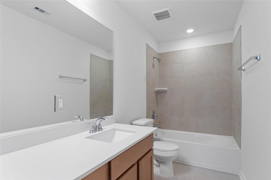 The secondary bathroom offers tile flooring, a bath/shower combination with a stylish tile surround, rich stained wood cabinetry, elegant light countertops, a mirror, and sleek fixtures with modern finishes. The secondary bathroom offers tile flooring, a bath/shower combination with a stylish tile surround, rich stained wood cabinetry, elegant light countertops, a mirror, and sleek fixtures with modern finishes.