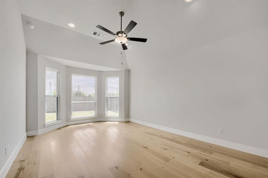 Spacious room featuring a bay window with three large windows, light wood-finish flooring, a modern ceiling fan, recessed lighting, and vaulted ceilings