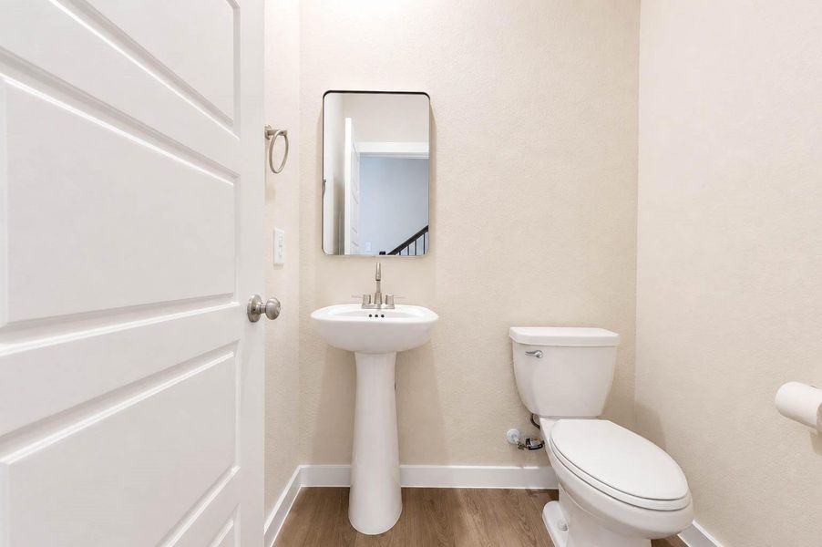 Convenient powder room features a clean, modern design with a pedestal sink, streamlined mirror, neutral finishes, and wood-look flooring. Its simple, polished aesthetic complements the rest of the home while providing an easily accessible guest bath on the main level. Convenient powder room features a clean, modern design with a pedestal sink, streamlined mirror, neutral finishes, and wood-look flooring. Its simple, polished aesthetic complements the rest of the home while providing an easily accessible guest bath on the main level.