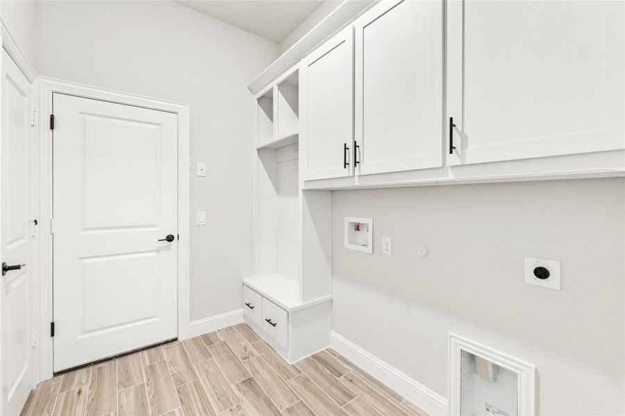 Mudroom with white upper cabinets, built-in bench with drawers, open cubbies, and washer hookups on wood-look tile floor. Mudroom with white upper cabinets, built-in bench with drawers, open cubbies, and washer hookups on wood-look tile floor.