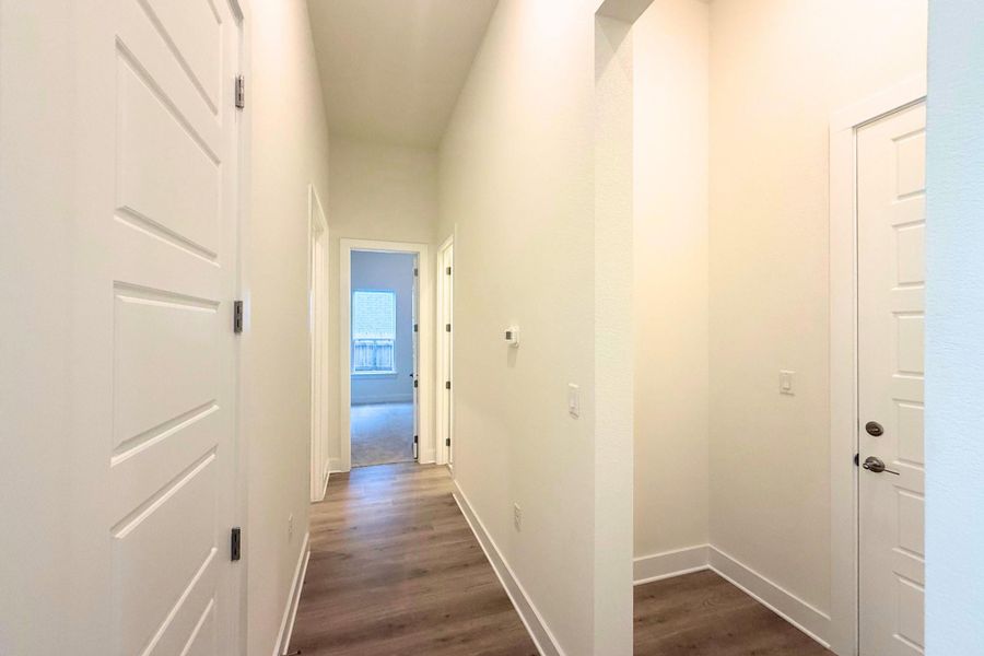 Hallway featuring wood-finish flooring, crisp white walls, and modern panel doors
