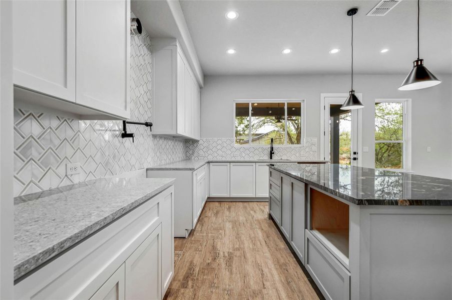 Kitchen featuring stone countertops, light wood-style flooring, visible vents, white cabinetry, and backsplash