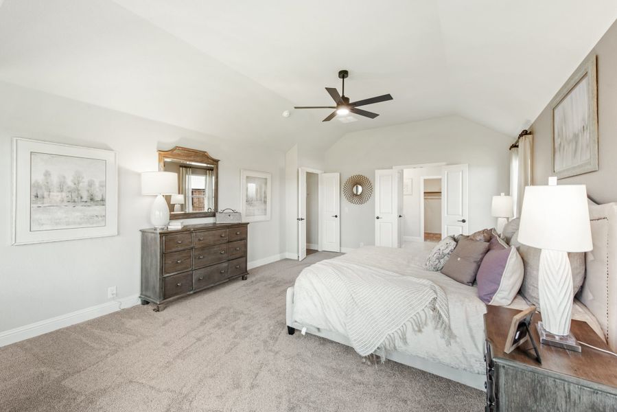 Master bedroom with vaulted ceiling, ceiling fan, carpet floors, and wood dresser with mirror