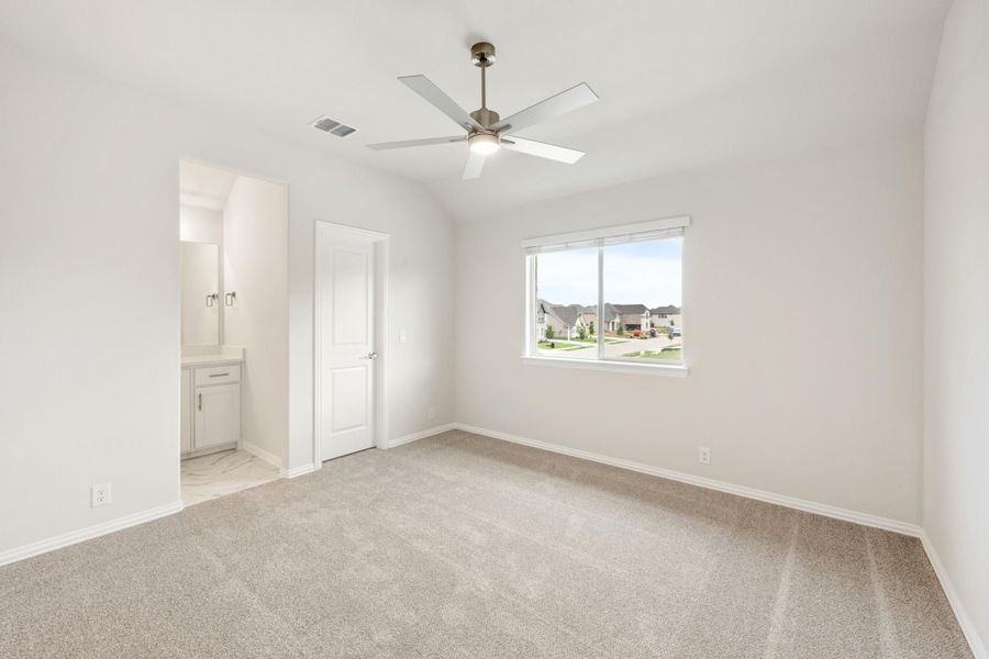 Empty bedroom with carpet, ceiling fan, vaulted ceiling, and ensuite bathroom entrance