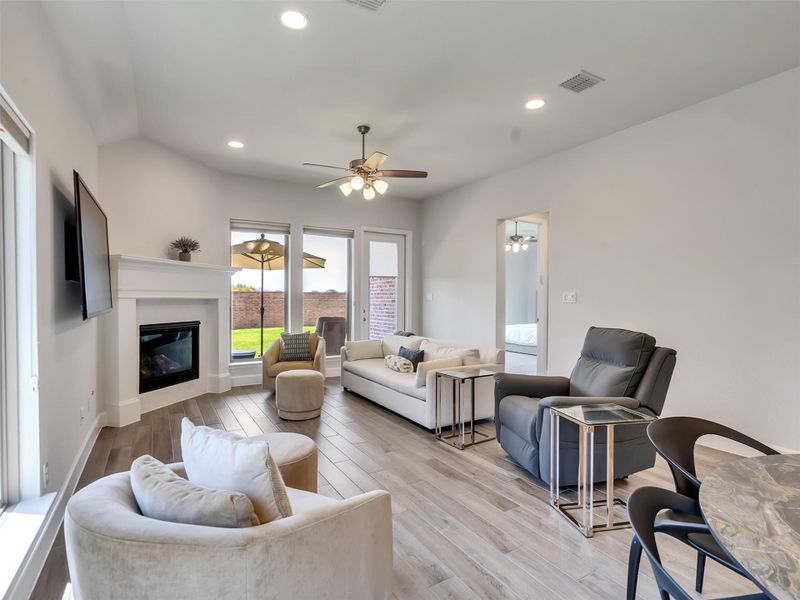Bright and inviting living area featuring a cozy fireplace, modern ceiling fan, and ample natural light from large windows.