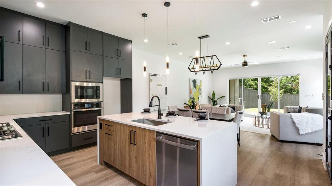 Kitchen with light hardwood / wood-style floors, stainless steel appliances, hanging light fixtures, sink, and a kitchen island with sink