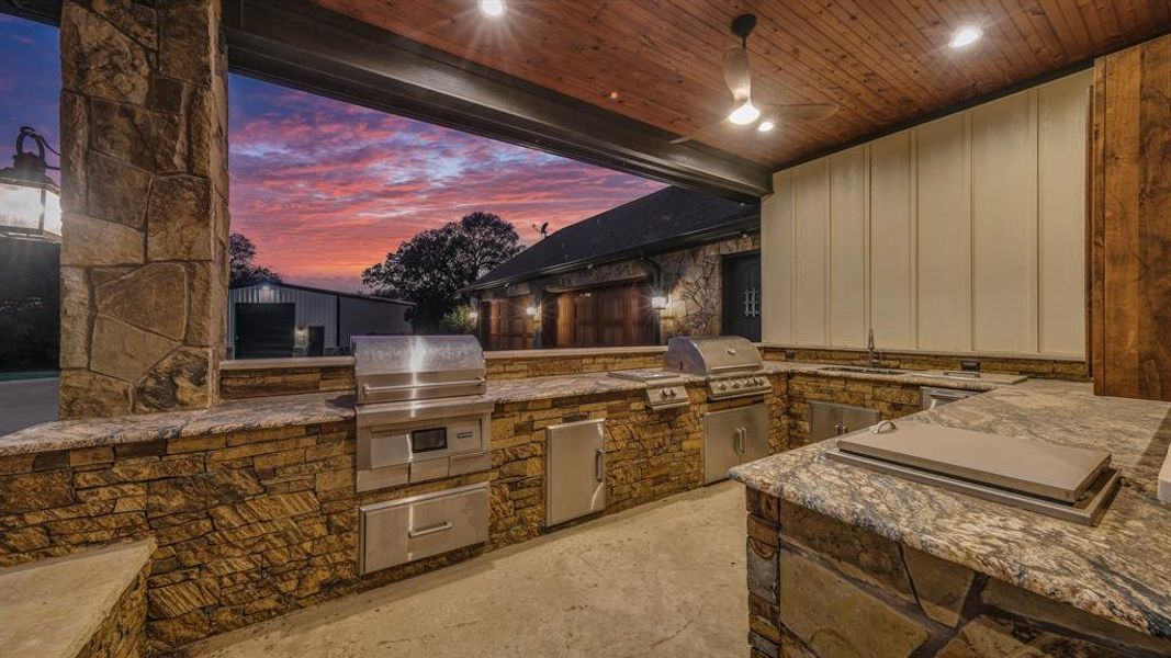 Built-in stone and granite kitchen with stainless steel appliances, grill, and prep space, ideal for entertaining.