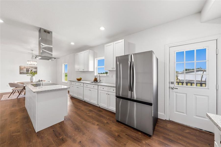 Contemporary kitchen featuring white cabinetry, light countertops, wood-finish flooring, a central island, and a stainless steel range hood