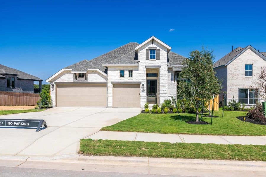 View of front facade with stone siding, driveway, a shingled roof, a garage, and brick siding