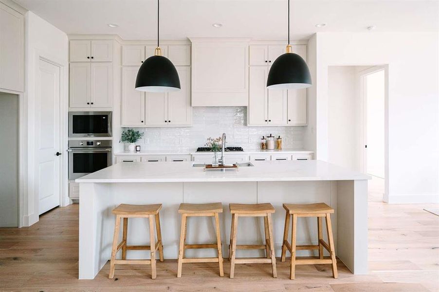 Kitchen with stainless steel oven, decorative backsplash, an island with sink, and white cabinetry