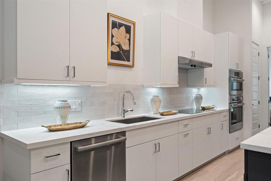 Kitchen featuring appliances with stainless steel finishes, decorative backsplash, under cabinet range hood, light wood finished floors, and white cabinets