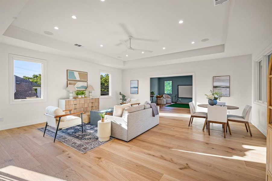 Living room with a wealth of natural light, a tray ceiling, ceiling fan, and light wood-type flooring