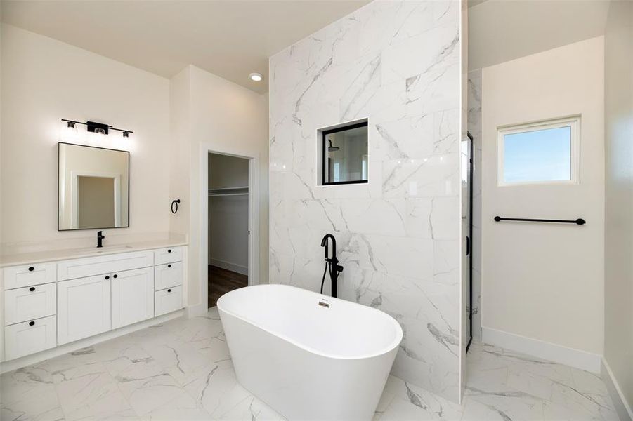 Full bath with stone wall, marble finish floor, a freestanding tub, and a walk in closet