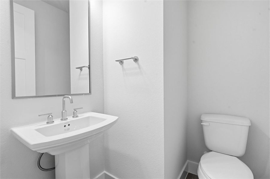 The first-floor powder room offers convenience and a modern aesthetic. It features a classic white pedestal sink complemented by a sleek faucet and a matching wall-mounted towel ring. A simple, large rectangular framed mirror enhances the sense of space and reflects the bright walls, making this half-bath both functional and stylish. The first-floor powder room offers convenience and a modern aesthetic. It features a classic white pedestal sink complemented by a sleek faucet and a matching wall-mounted towel ring. A simple, large rectangular framed mirror enhances the sense of space and reflects the bright walls, making this half-bath both functional and stylish.