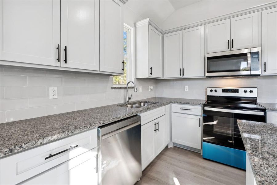 Kitchen featuring sink, appliances with stainless steel finishes, light hardwood / wood-style floors, light stone counters, and white cabinetry