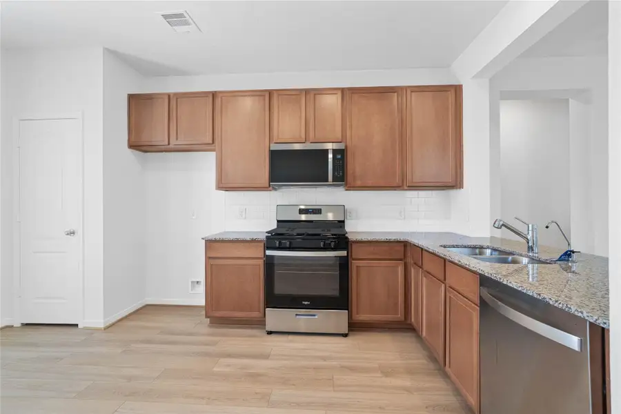 This open kitchen boasts soaring ceilings, Woodmont Cody cabinets in Toffee stain, Granite countertops in Caramel Cream, stainless steel Whirlpool appliances, a modern Daltile backsplash, recessed lighting, and a pantry—all overlooking the expansive family room. This open kitchen boasts soaring ceilings, Woodmont Cody cabinets in Toffee stain, Granite countertops in Caramel Cream, stainless steel Whirlpool appliances, a modern Daltile backsplash, recessed lighting, and a pantry—all overlooking the expansive family room.