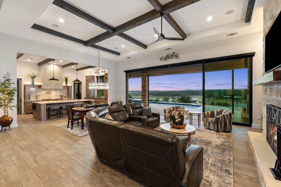 The open-concept living area features soaring ceilings with dark timber beams and massive sliding glass walls that frame breathtaking, long-range views of Lake Travis.