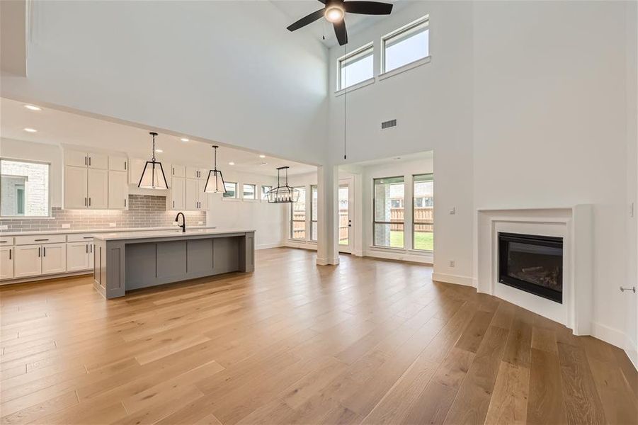 Unfurnished living room featuring sink, light hardwood / wood-style flooring, ceiling fan, and a high ceiling