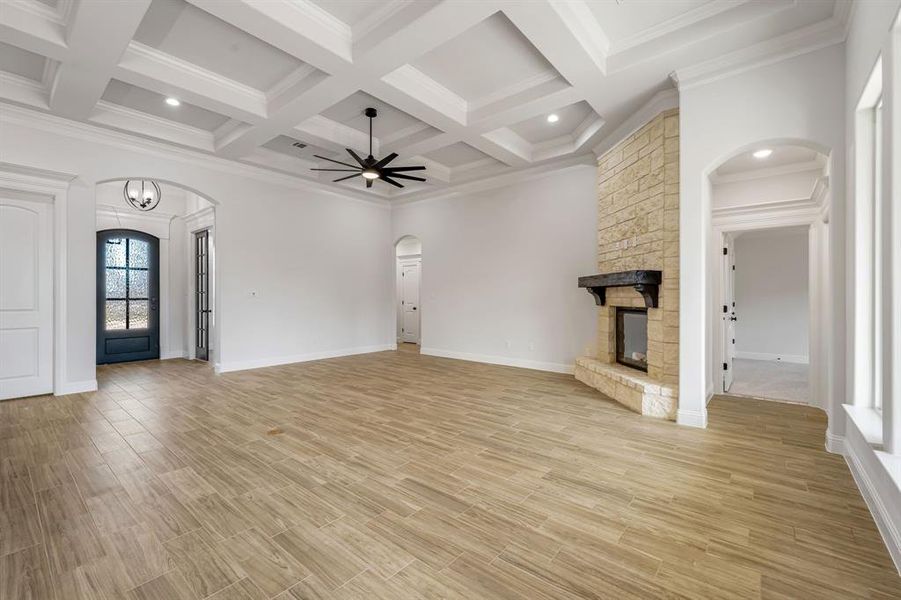 Unfurnished living room with a fireplace, beam ceiling, coffered ceiling, ornamental molding, and ceiling fan with notable chandelier