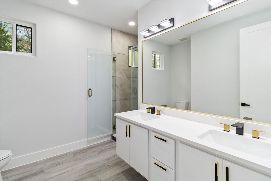 Full bath featuring double vanity, a stall shower, light wood finished floors, and recessed lighting