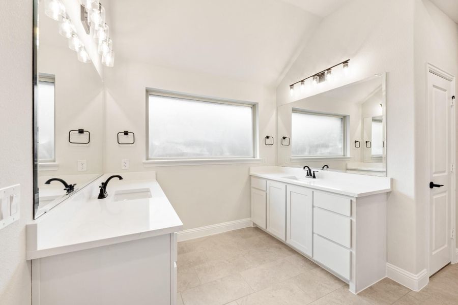 Bathroom with dual vanities, white cabinets, black fixtures, and vaulted ceiling Bathroom with dual vanities, white cabinets, black fixtures, and vaulted ceiling