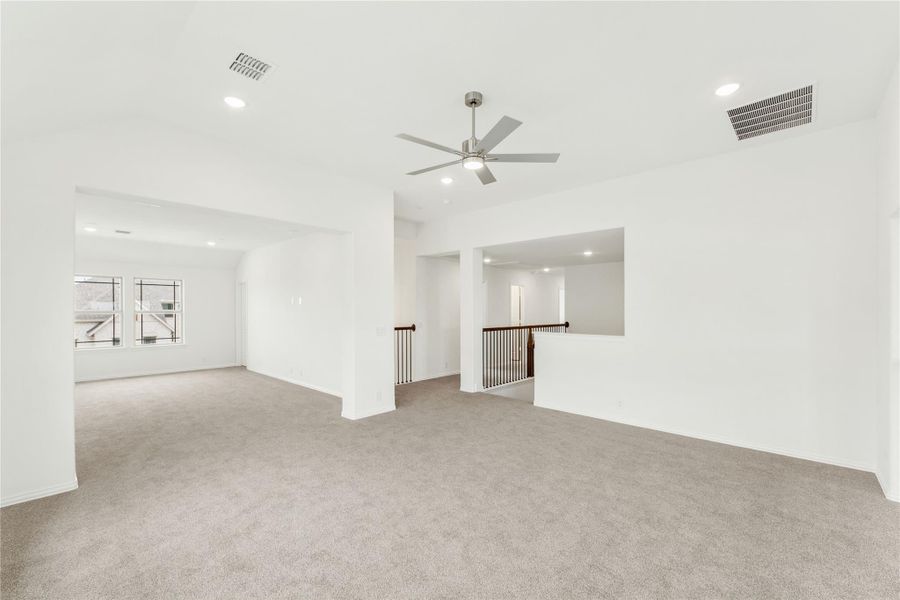 Spacious upstairs living area with carpet, ceiling fan, and open staircase railing