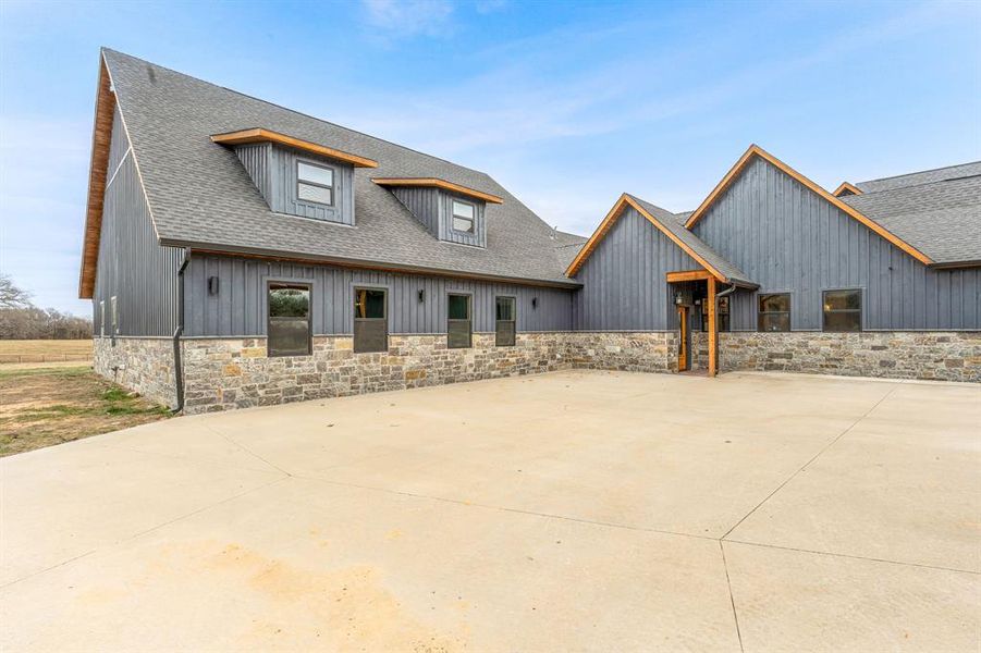 View of front facade featuring stone siding, a shingled roof, and board and batten siding
