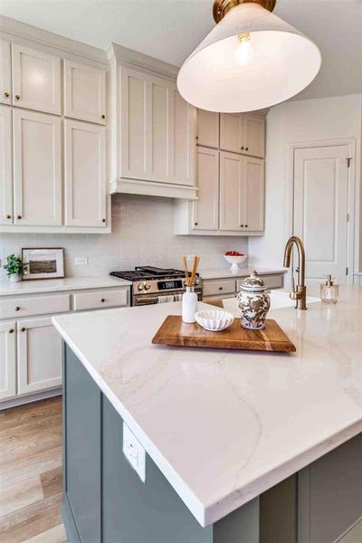 Kitchen featuring gray cabinetry, decorative backsplash, light stone counters, gas range, and a center island Kitchen featuring gray cabinetry, decorative backsplash, light stone counters, gas range, and a center island