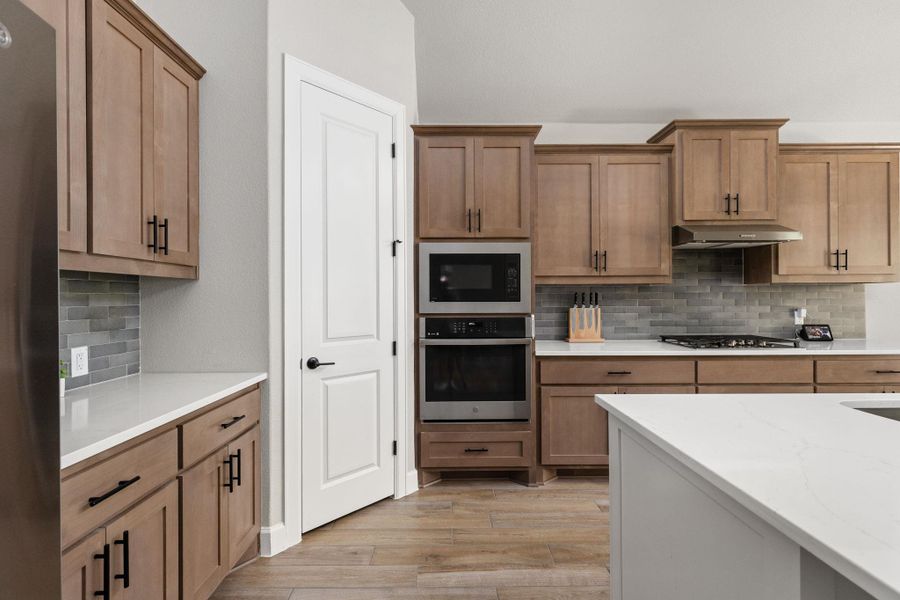 Kitchen featuring backsplash, stainless steel appliances, light stone countertops, and light brown cabinetry