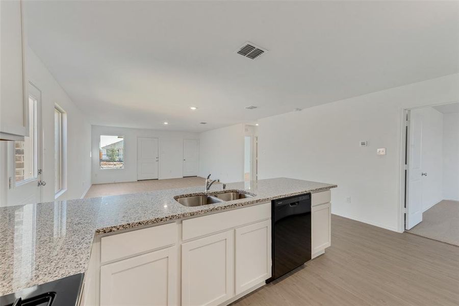 Kitchen featuring white cabinets, dishwasher, light stone countertops, and sink